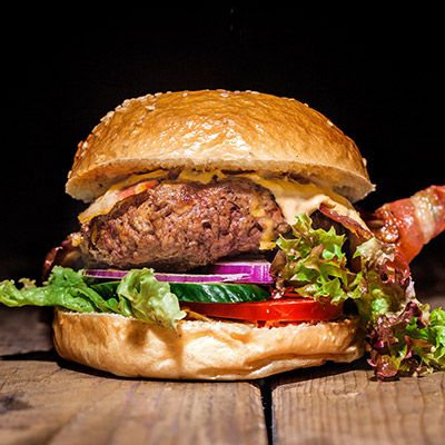 Burger mit Bacon, Salat und Tomate auf Holzbrett