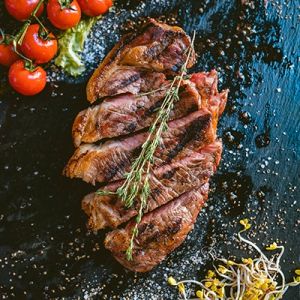 Gegrilltes Steak mit Thymian und Tomaten auf dunklem Schiefer