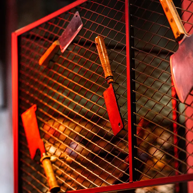 Grillwerkzeug an einem roten Gitter vor dem Feuer